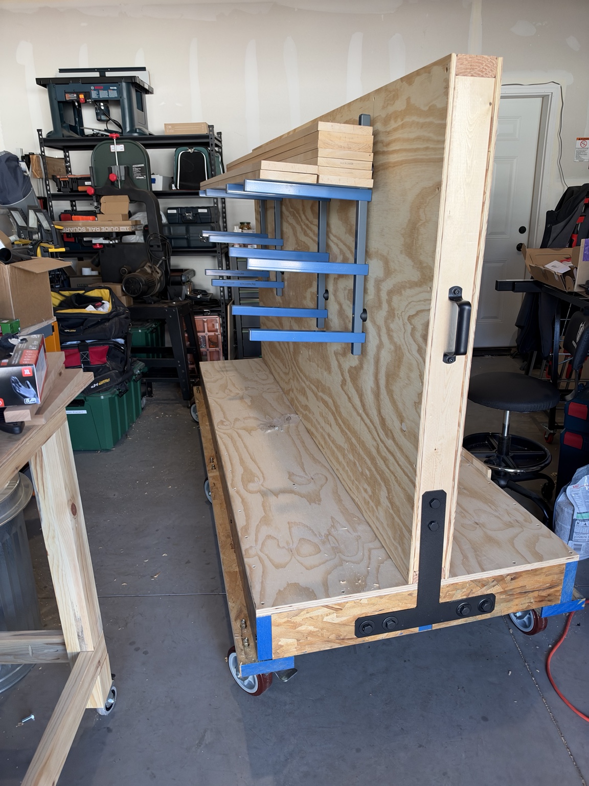 Blue six-tier rack arms mounted to the plywood wall, with black end strap and handle