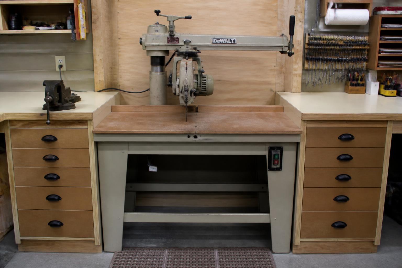 Radial arm saw mounted front-facing in its cabinet bay with the table flush to the worktops on both sides
